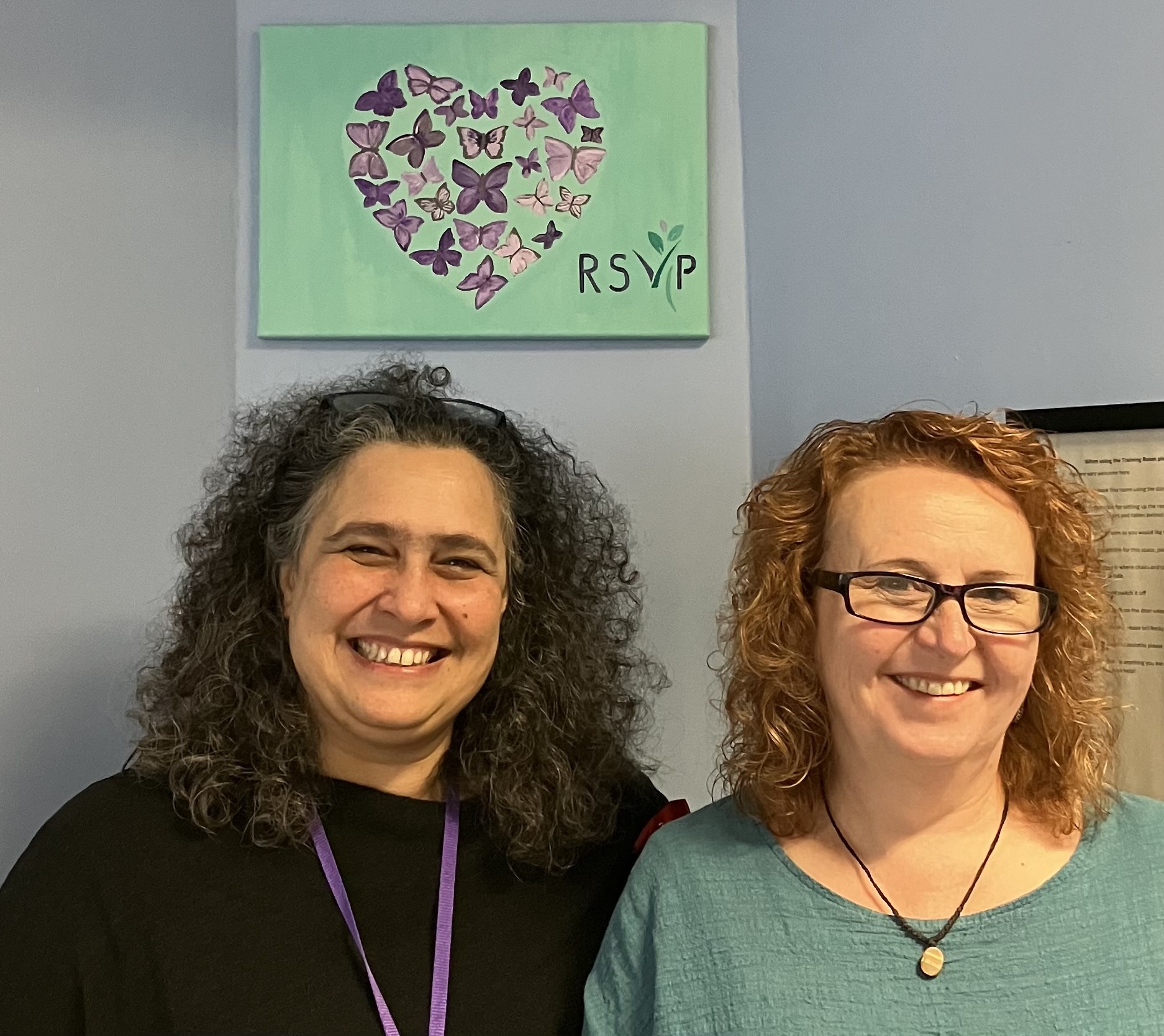 A photo of two smiling women beneath a heart shape, made of heart butterflies. 